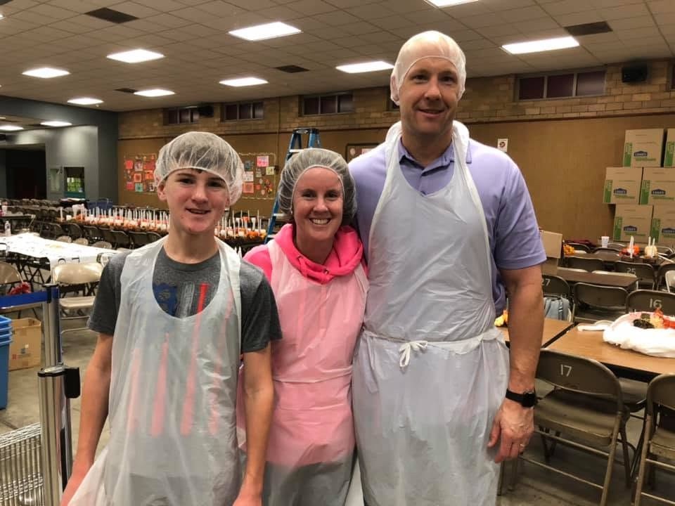 Three dinner volunteers smiling together in aprons and hair coverings.